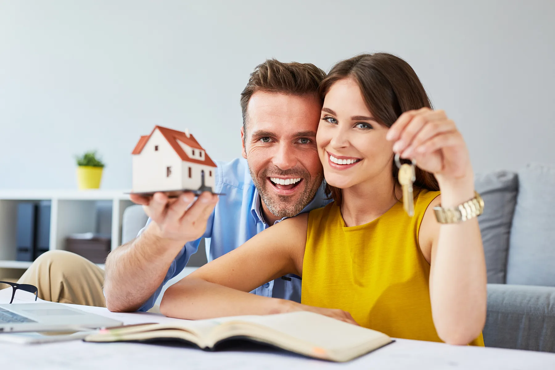 Casal sorrindo no sofá com uma miniatura de casa